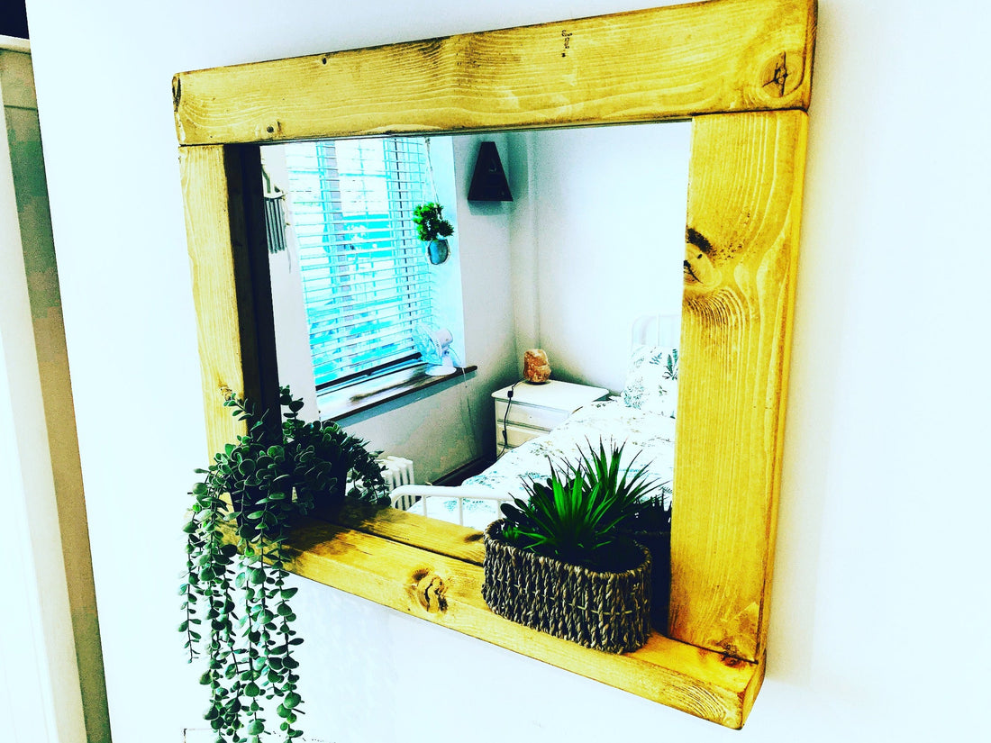 Rustic wooden shelf mirror with two plants, reflecting a bedroom window and bed