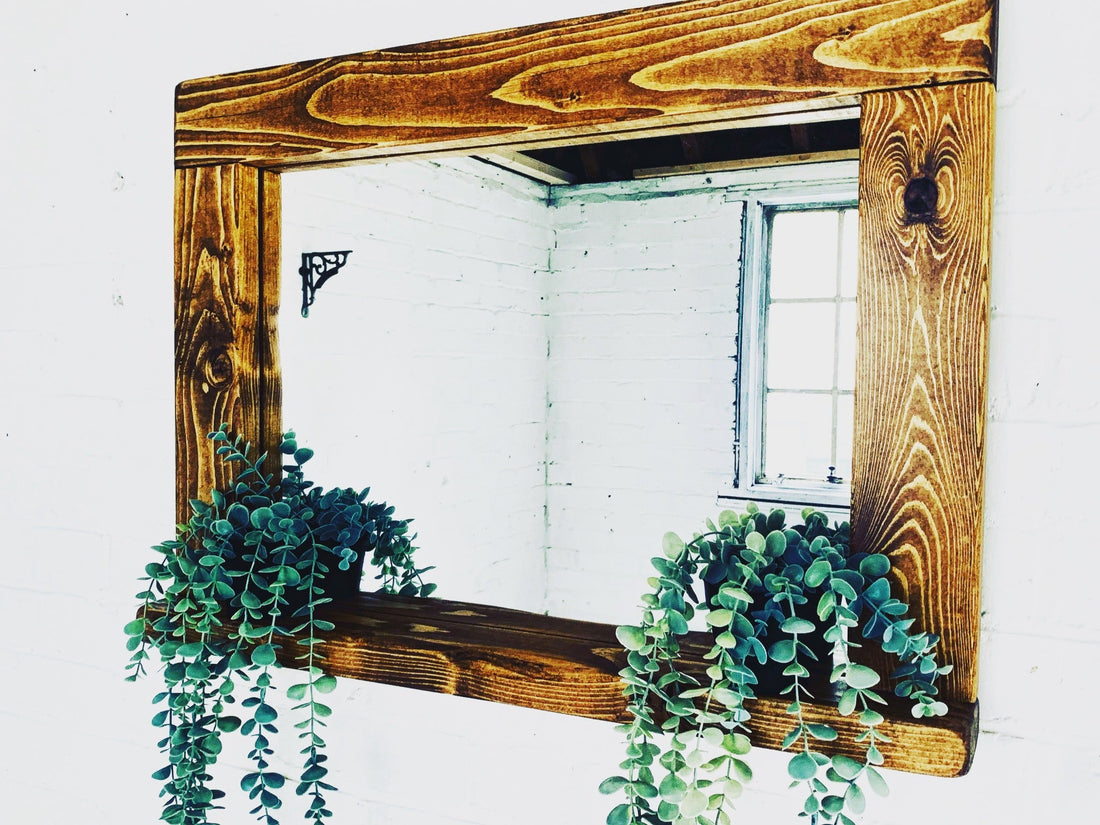 Rustic wooden shelf mirror with prominent grain and two trailing plants against a pale brick wall