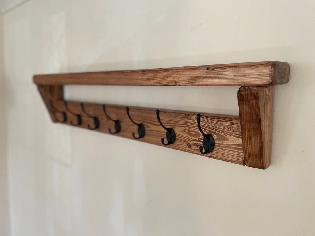 Long rustic wooden coat rack with ten black hooks mounted on a wall