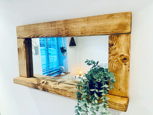 Rustic wooden mirror with shelf and a trailing plant, shown against a pale wall